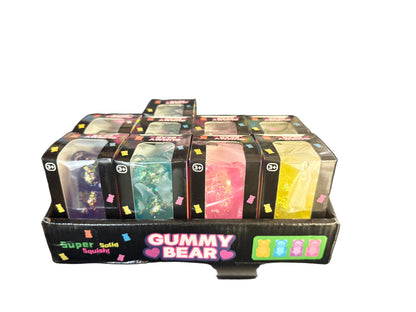 A retail display box filled with multiple small packages of glittery gummy slime, labeled 'GUMMY BEAR' and 'Super Solid Slime,' photographed indoors on a black stool.